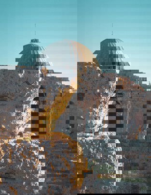 صورة لقبة معمارية بارزة وهيكل حجري قديم، يظهر في الخلفية سماء زرقاء صافية