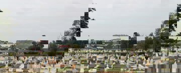 مشروع صدقة جارية للميت منظر واسع لمقبرة إسلامية تحتوي على قبور مرتبة بعناية، معظمها أبيض اللون ويحتوي على شواهد مزخرفة. تظهر في الخلفية أشجار ومباني وتل تعلوه قبة بيضاء بارزة.